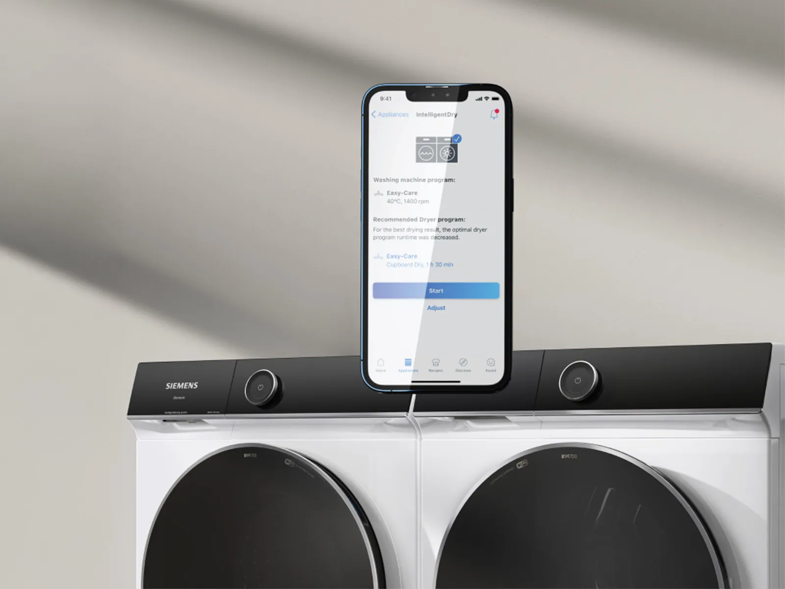 Smartphone avec application Siemens Home Connect sur lave-linge et sèche-linge.