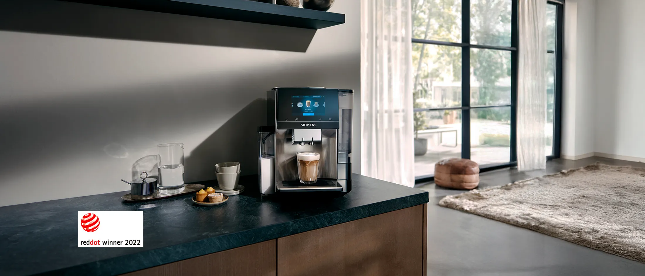 מכונת קפה מודרנית של Siemens על דלפק המטבח עם כוס קפה טריה, חטיפים ולוגו זוכה רד דאט 2022.