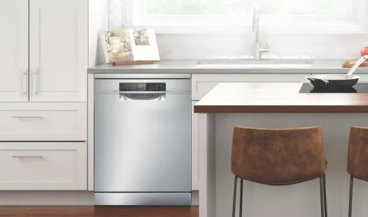 A stainless steel Bosch dishwasher integrated into a modern kitchen with white cabinets and a counter with a sink and bar stools.