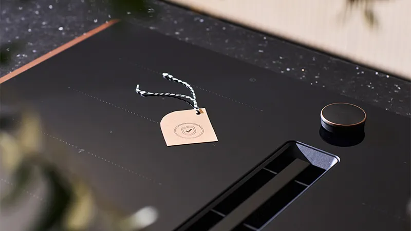 alt-Beige label with red and white string on a black NEFF hob and plants blurred in the foreground.