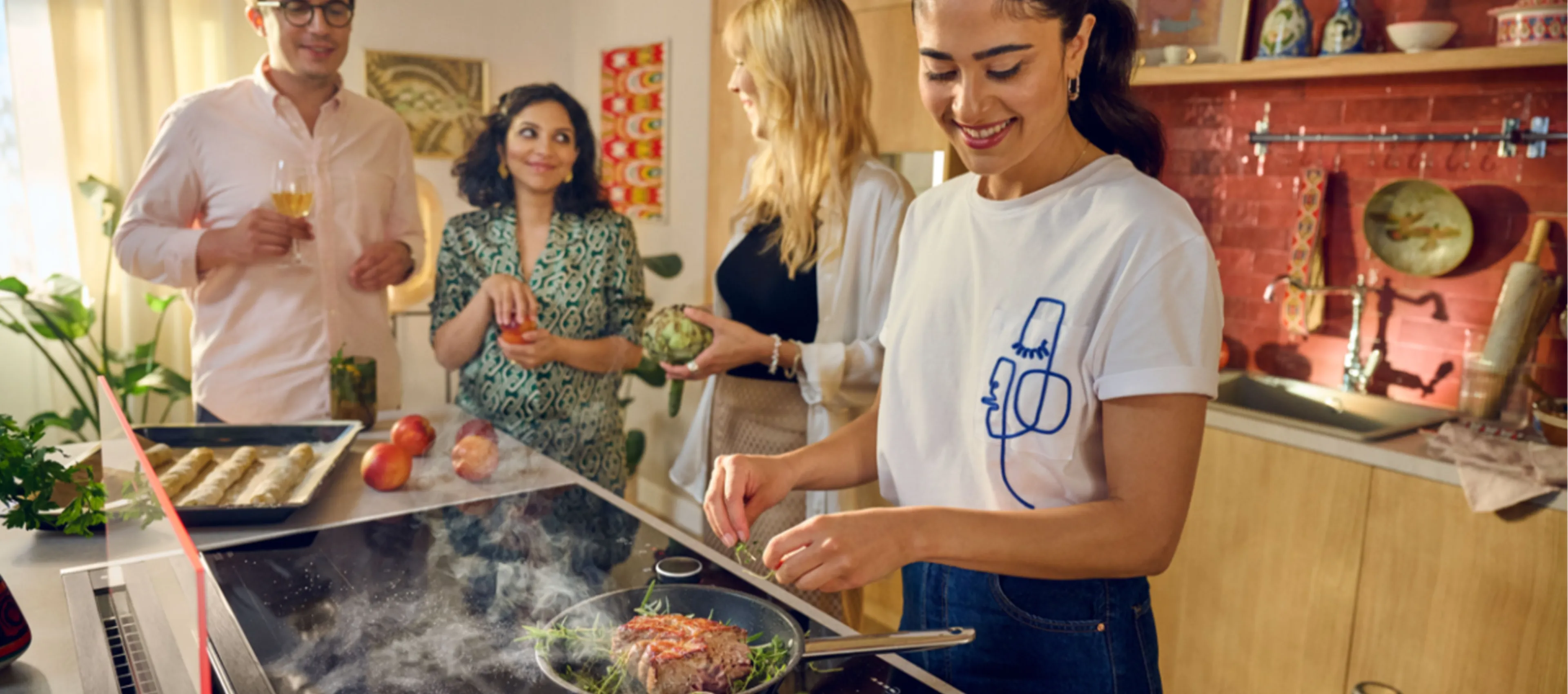 A group of people cooking in a kitchen with a glass draft hood, preparing various dishes together.  