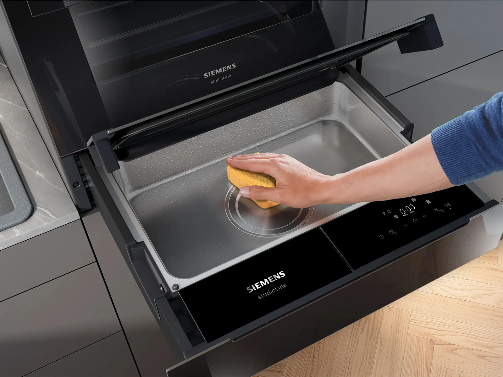 Una persona pulisce l'interno di un forno Siemens studioLine con una spugna gialla in una cucina moderna.
