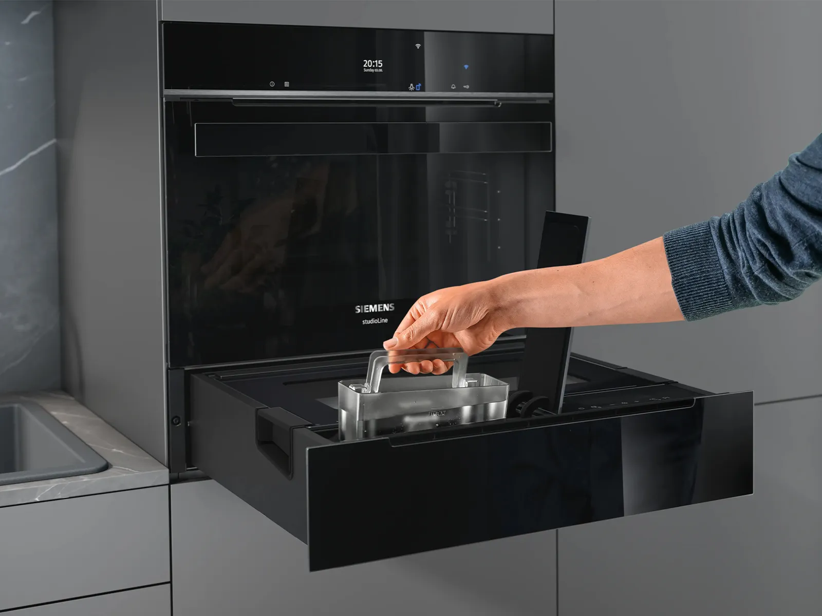 Una persona utilizza un forno Siemens con cassetto scorrevole, situato in un ambiente cucina moderno.