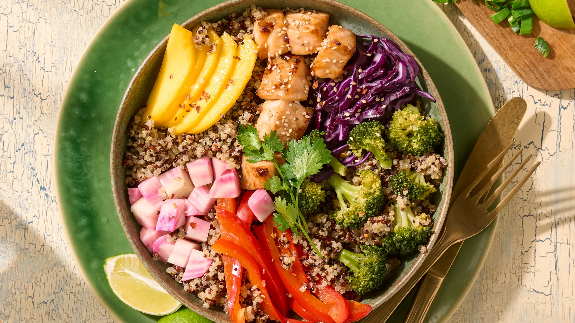 Bunte Quinoa-Bowl mit Lachs, Brokkoli, Mangoscheiben, Rotkohl, Paprika und gewürfelten Beten auf einem grünen Teller.