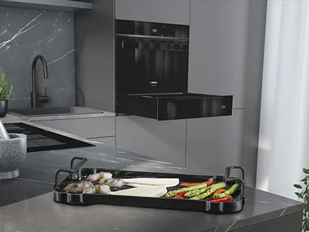 Modern kitchen with a black countertop tray holding assorted vegetables and seafood.