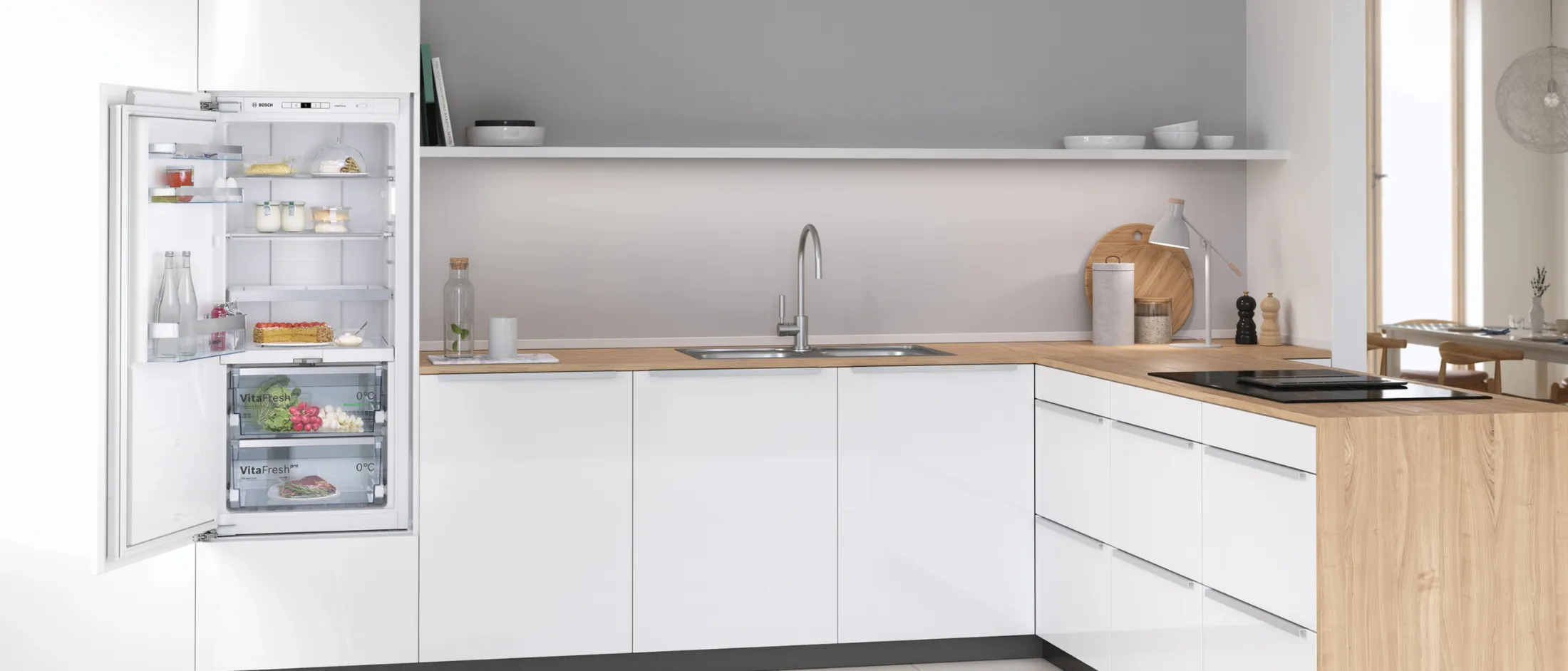 مطبخ عصري بخزائن بيضاء، وطاولة عمل خشبية فاتحة اللون، ومغسلة وصنبور من الفولاذ المقاوم للصدأ.