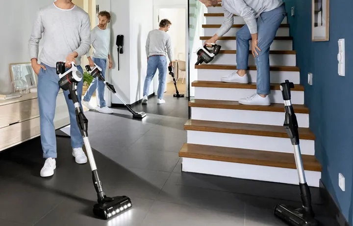 A composite image showing a man using a Bosch cordless vacuum cleaner in three different ways: as a stick vacuum on a dark floor, as a handheld vacuum on stairs, and another instance of him walking with the stick vacuum.