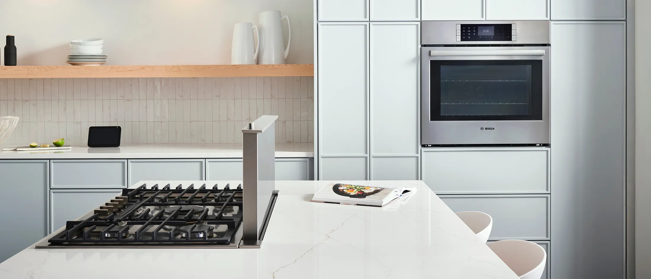 Modern kitchen featuring a gas stove, built-in Bosch oven, minimalist cabinetry, and stylish decor, with fresh limes and a cookbook.