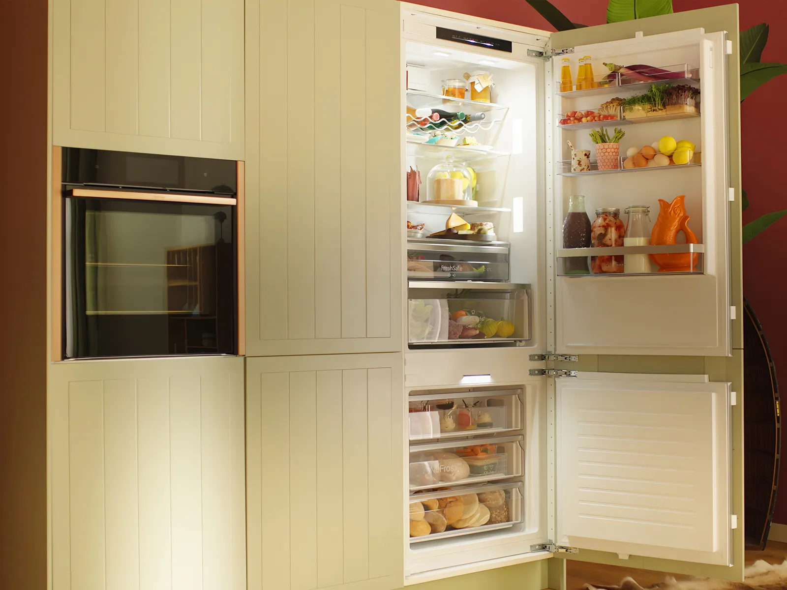Ein moderner, hellgrüner Kühlschrank mit offenen Türen, hinter denen übersichtlich angeordnete Lebensmittel und Getränke zu sehen sind, vor einer leuchtend roten Wand.