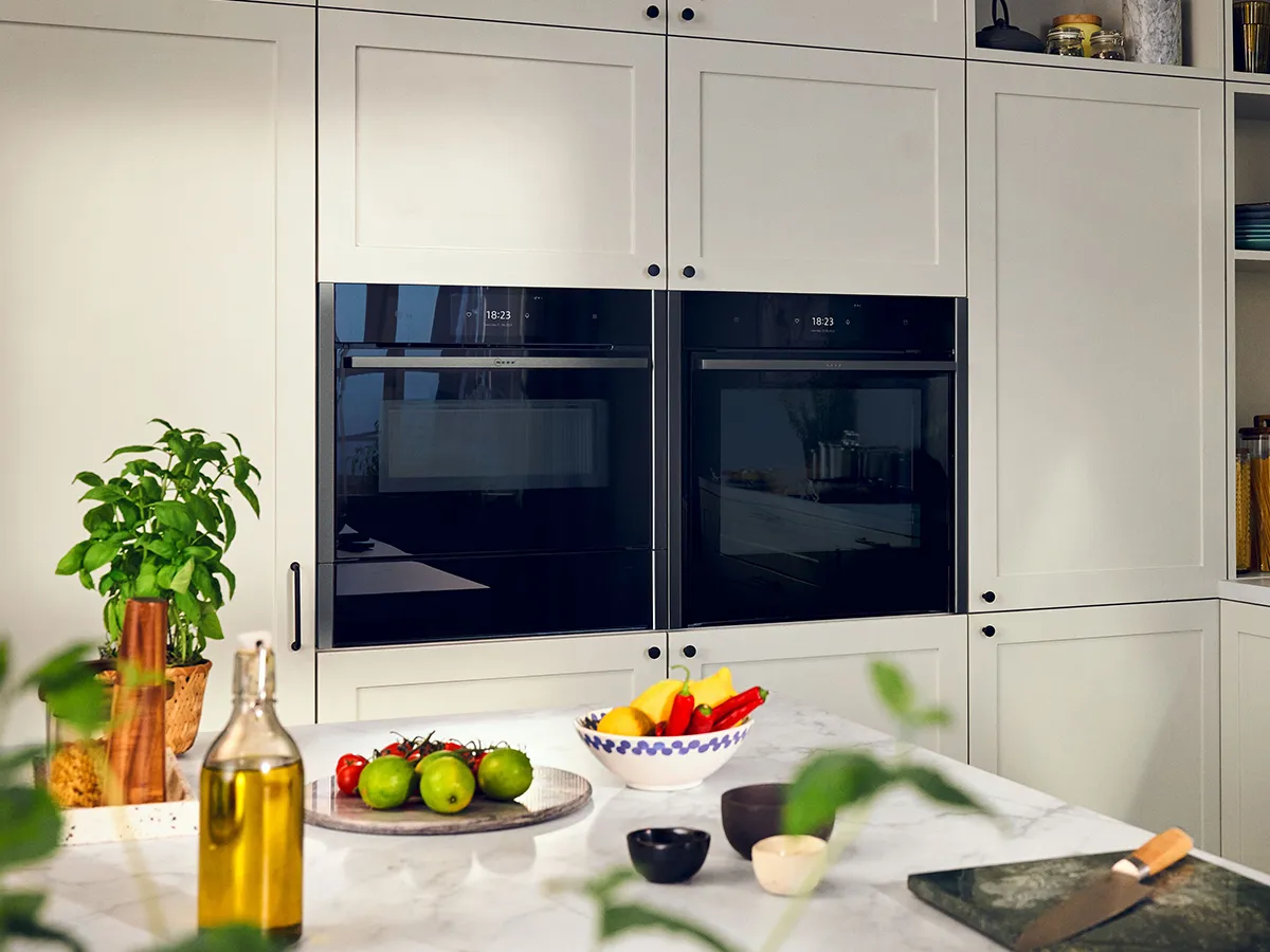 A sleek modern kitchen with a built-in black oven and cream cabinetry, featuring knobs and a digital display on the oven's front for steering oven and cooktop above.