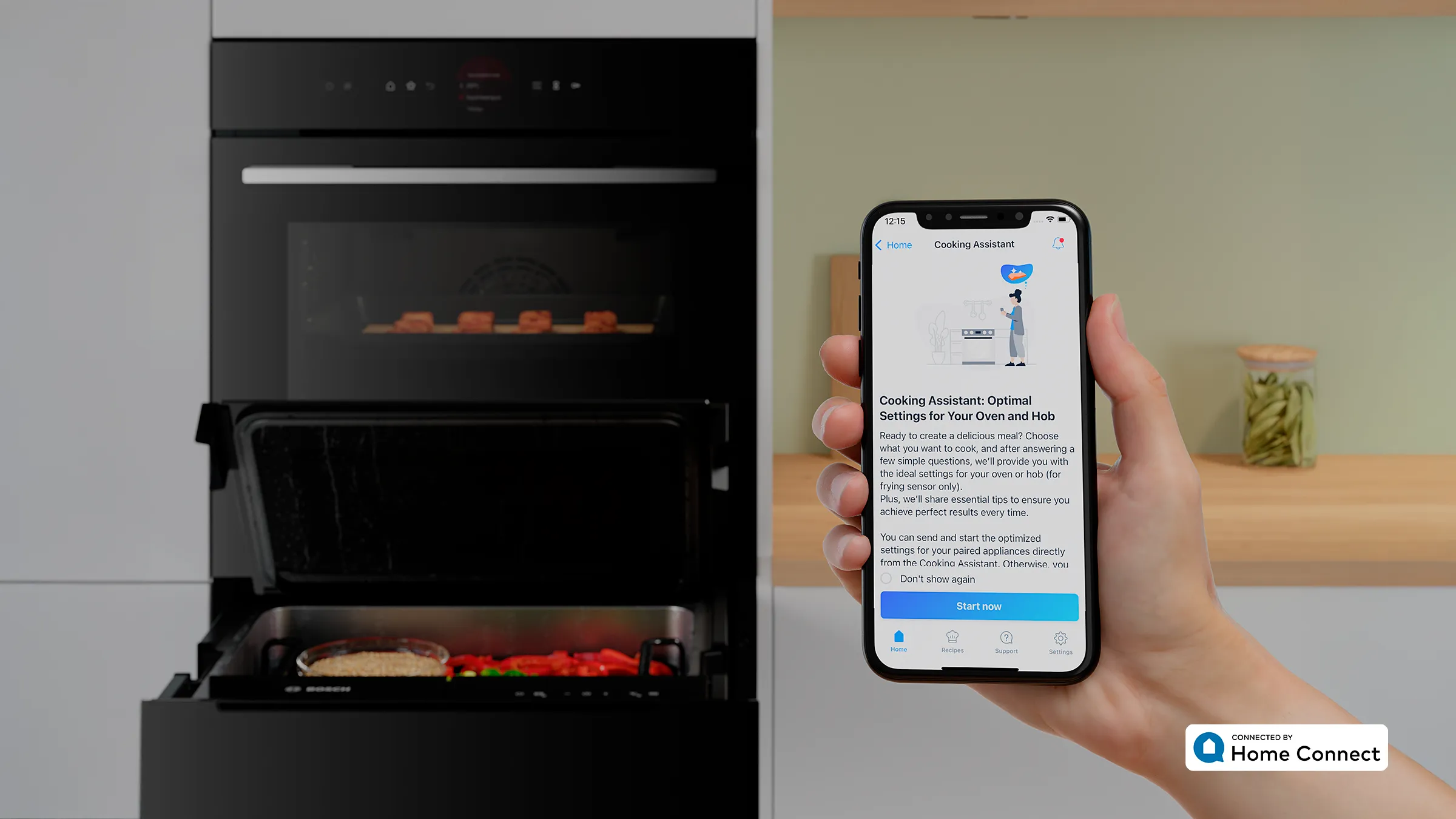 Eine Hand hält ein Smartphone mit dem geöffneten Home Connect ‚Cooking Assistant‘ vor einer Gerätekombination aus Bosch Serie 8 Backofen und Dampfgarer-Schublade.