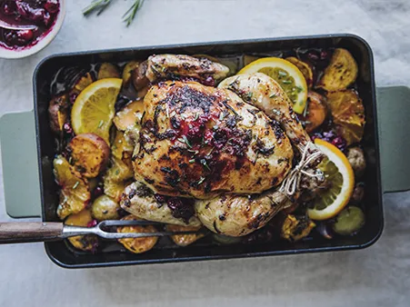 Goldbraunes Brathähnchen mit Zitronenscheiben und Gemüse in einer schwarzen Backform.