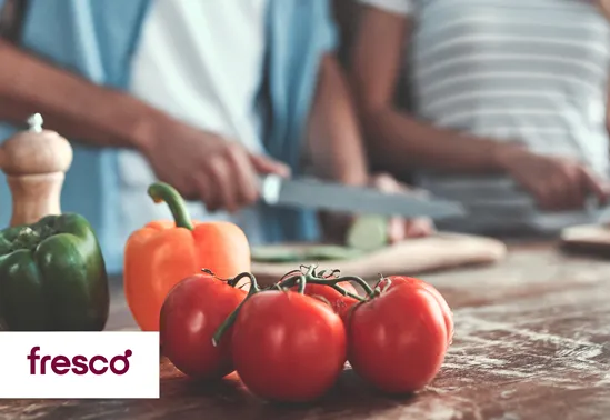 People cooking with fresh tomatoes and bell peppers on a wooden kitchen table.