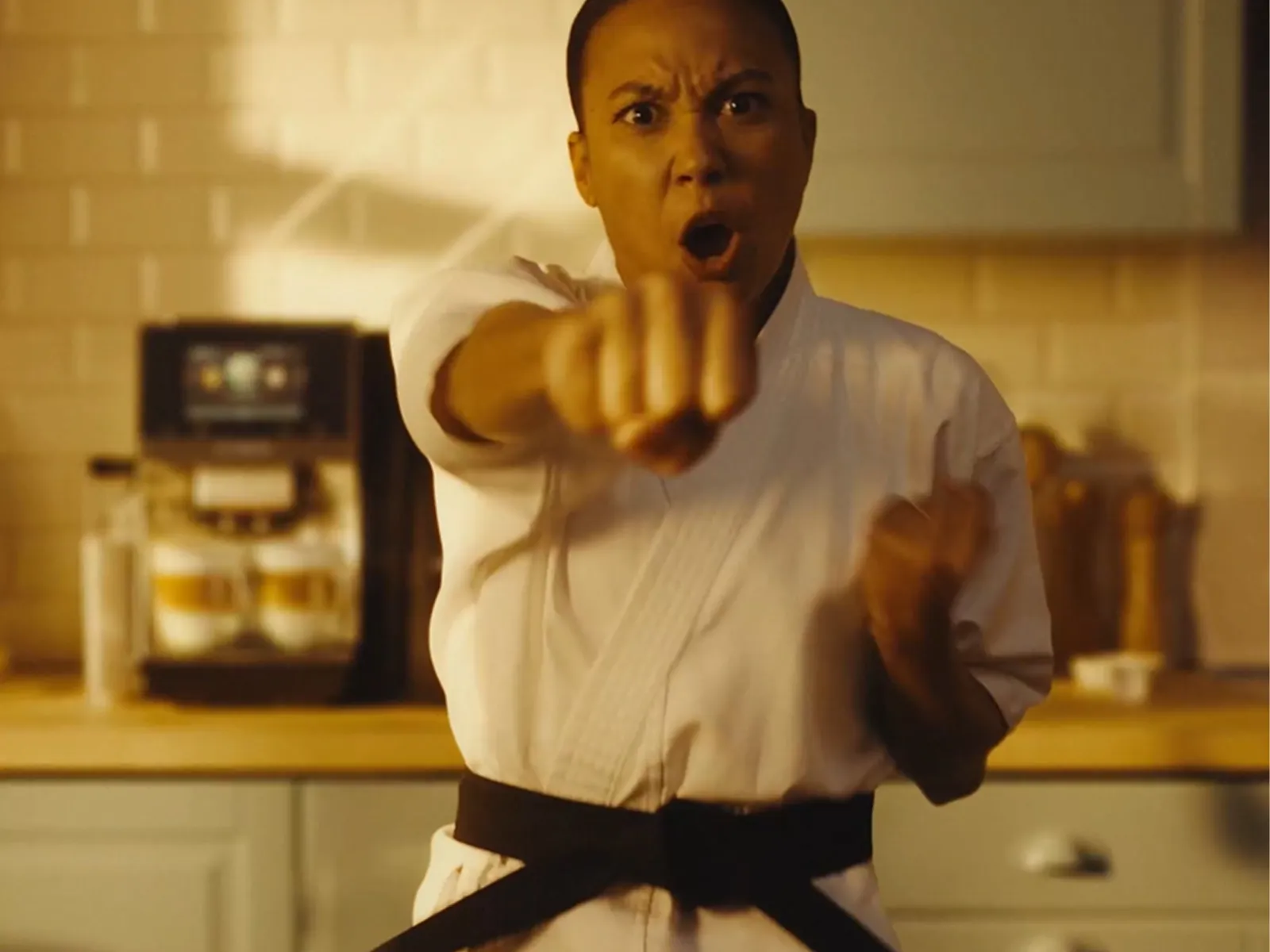 A sleek coffee machine serves a latte in a glass cup, beside a wooden stand with cookies and a mug, in a bright kitchen setting.