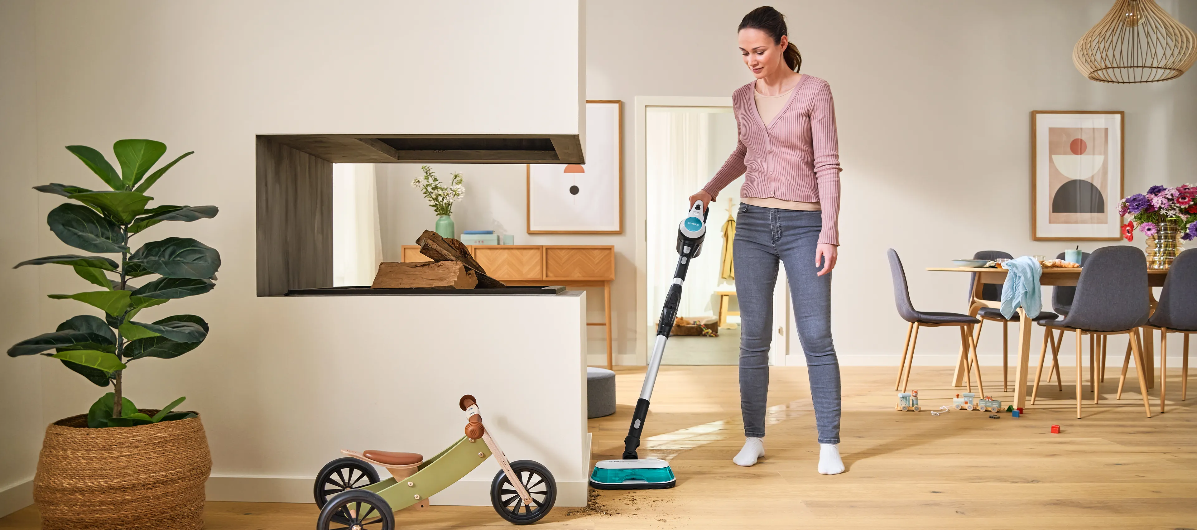 Naine puhastab põrandat heledas, modernses eluruumis, kus on potitaim ja puidust söögilaud, mis on kaunistatud lilledega