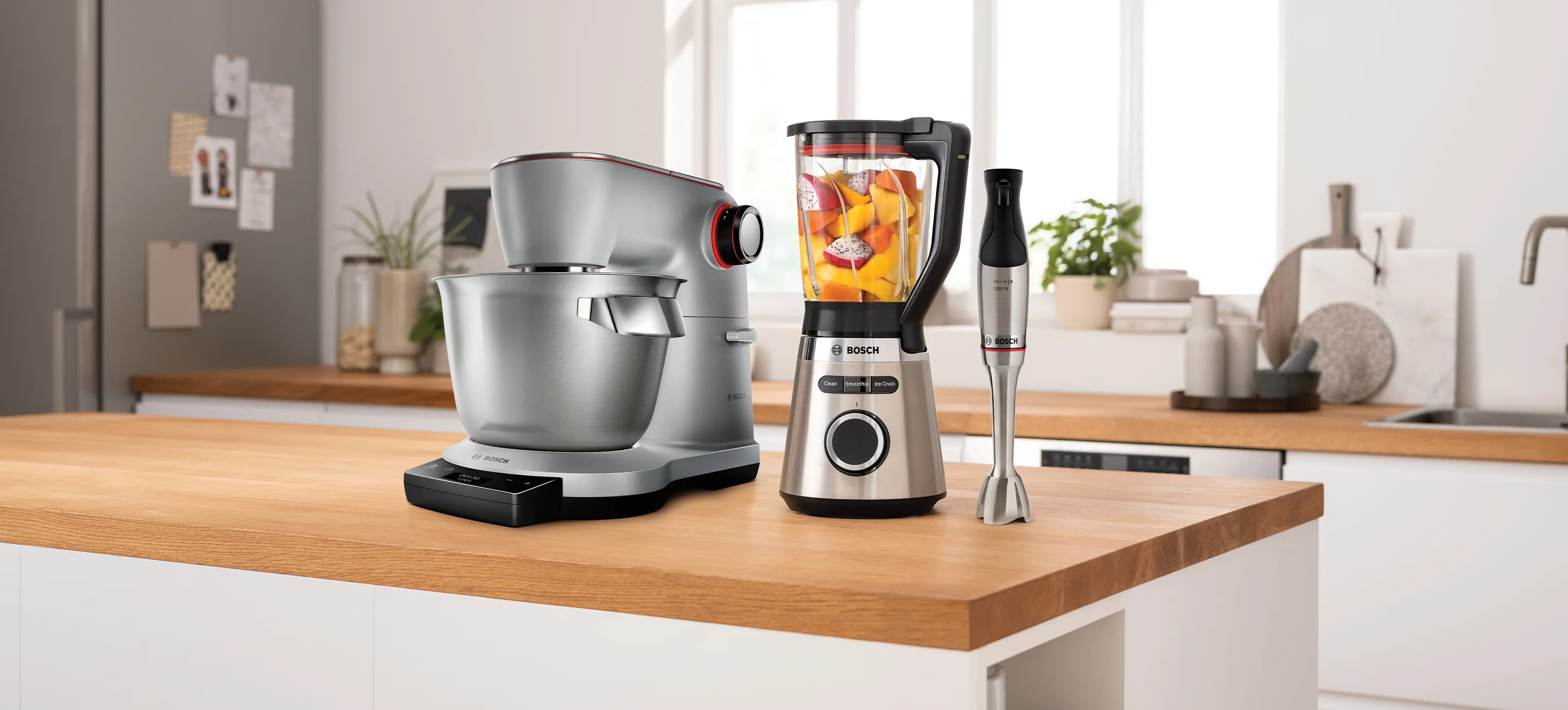 Moderne köögistseen hõbedase stand-mikseri, klaasist blenderi, milles on puuviljad, ja käsi-blenderiga puidust töötasapinnal.