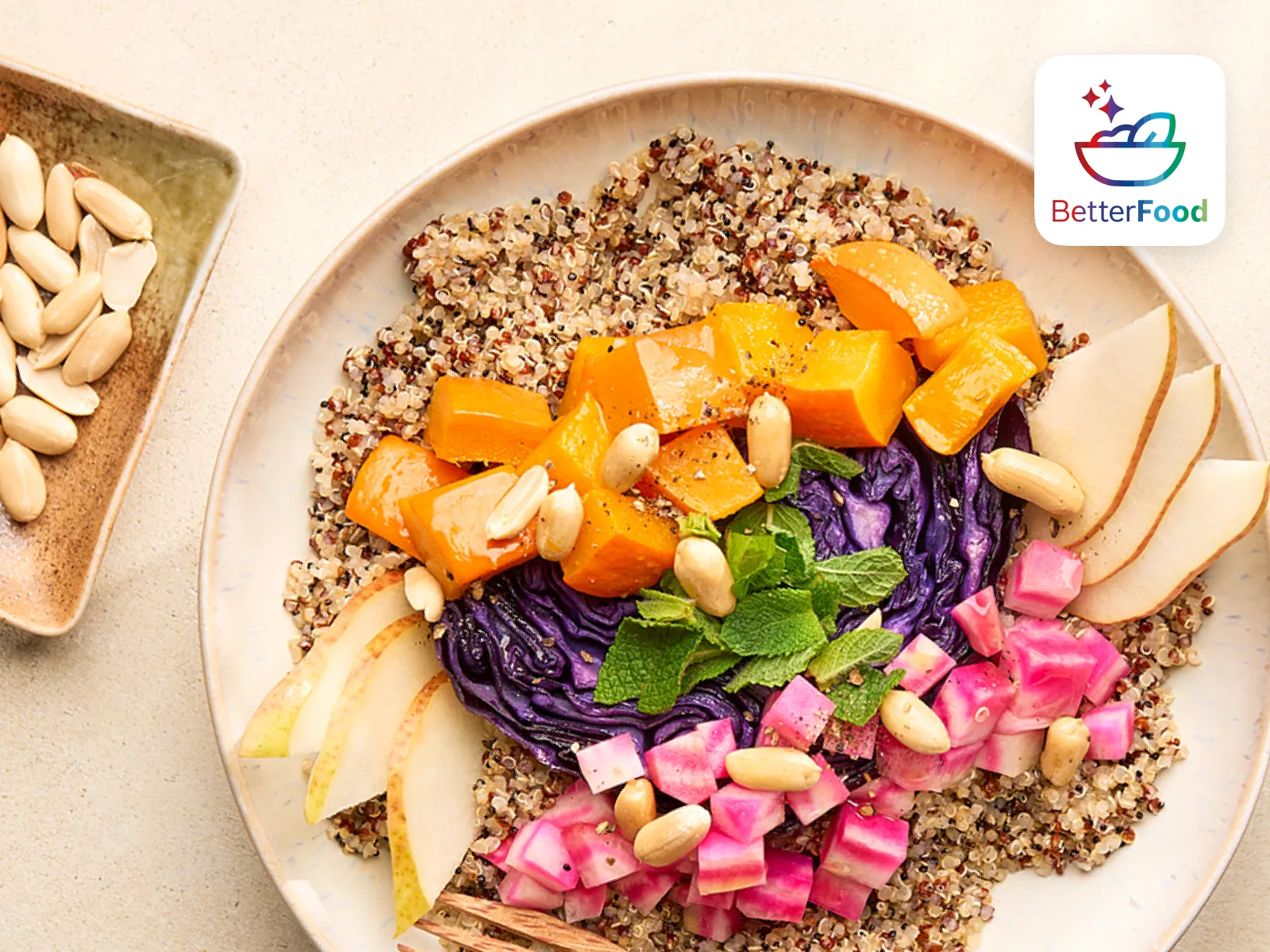 Eine bunte Quinoa-Bowl mit gebackenem Kürbis, Rotkohl, eingelegtem Gemüse, Birnenscheiben und Erdnüssen auf einem großen Teller.