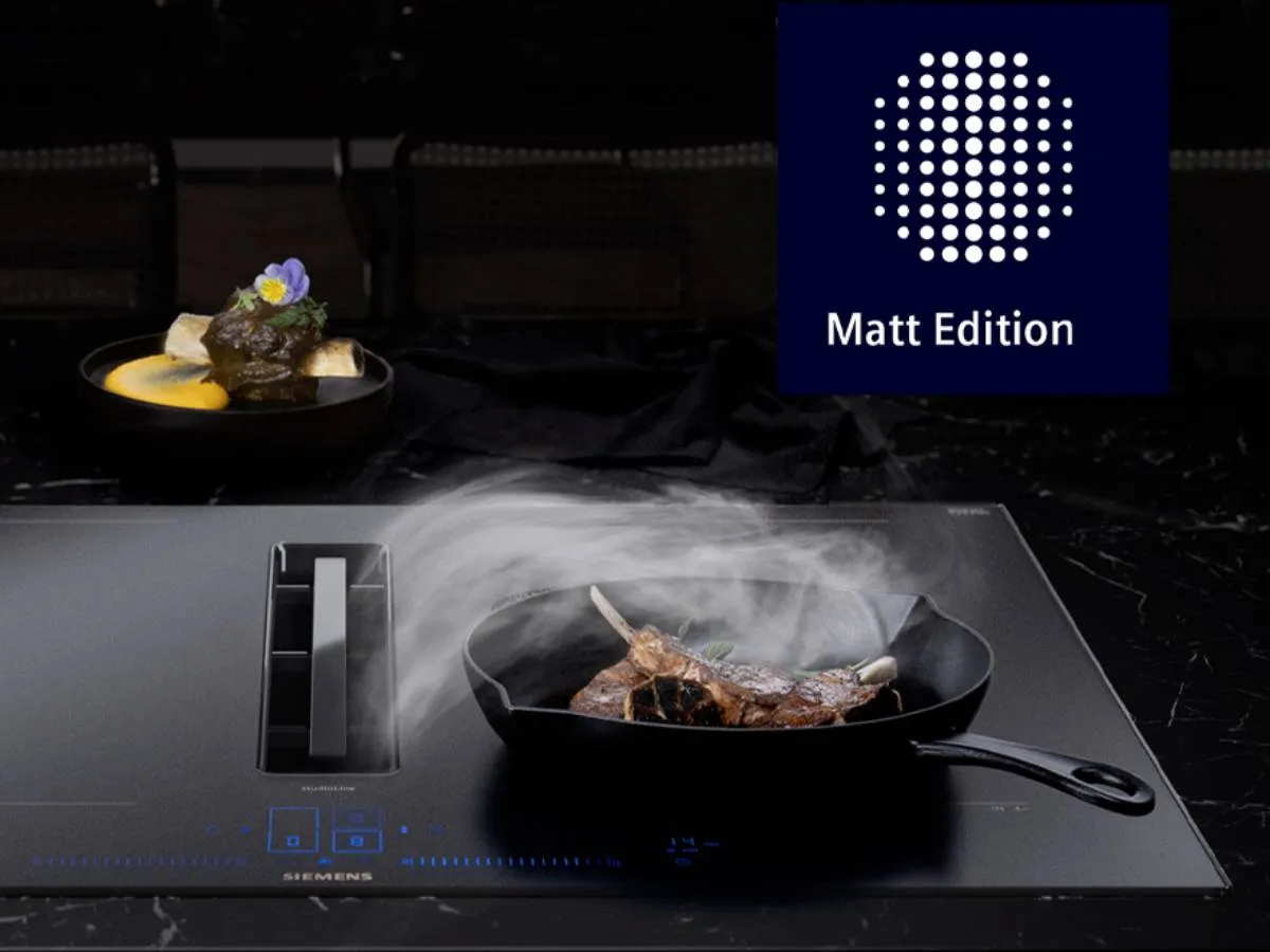 Auf einem eleganten, schwarzen Induktionskochfeld brutzelt ein Steak in einer Pfanne, über dem Rauch aufsteigt, und daneben steht in einer Schüssel ein Gourmetgericht