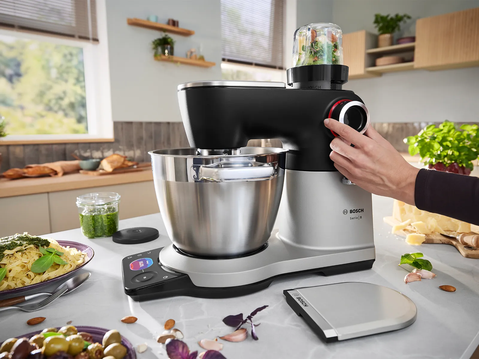 Le robot pâtissier de la Série 8 est posé sur un plan de travail entouré d'aliments pendant l'utilisation de la fonction hachoir et qu'une main règle le cadran du robot pâtissier.