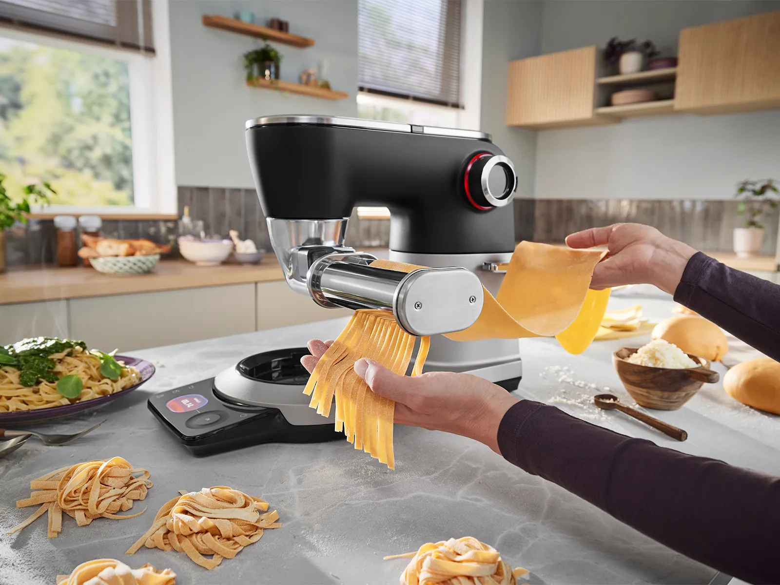 Le robot pâtissier Series 8 est posé sur un plan de travail, entouré de produits et d’ingrédients pour pâtes, pendant qu’une personne utilise l’accessoire pâtes pour les découper.