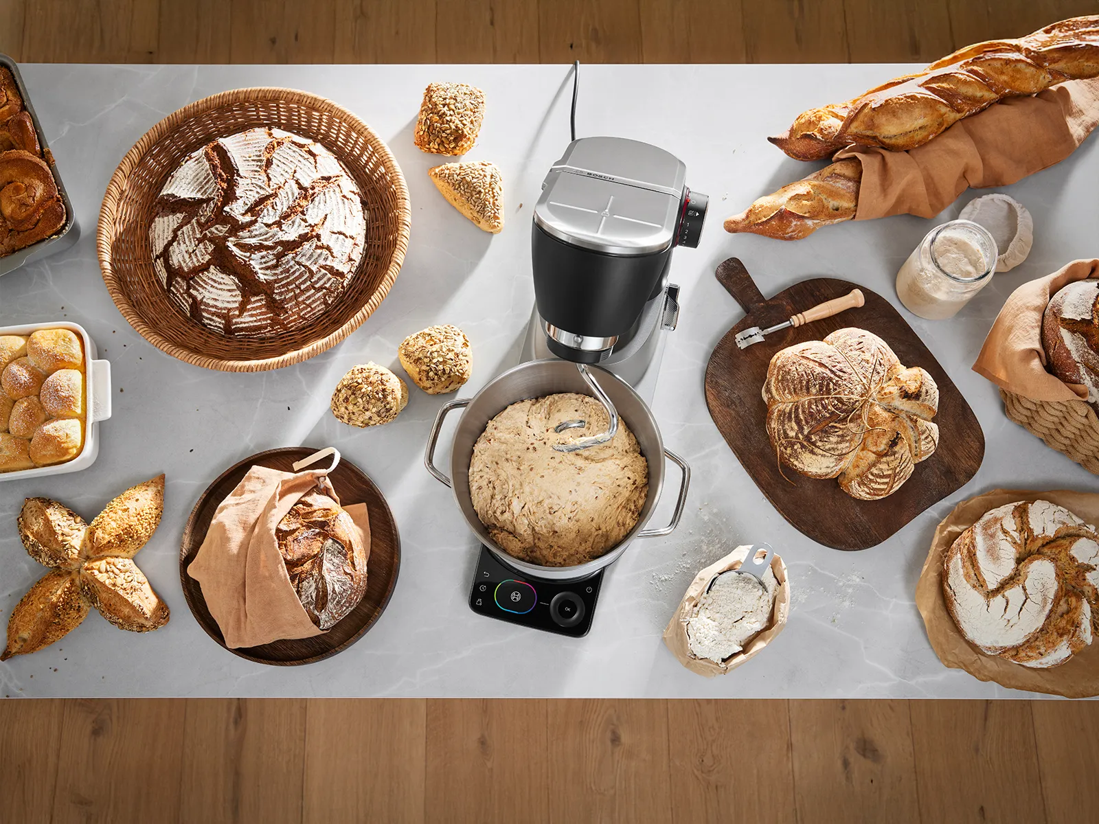 Various types of bread and pastries on a marble counter with a black stand mixer kneading dough.