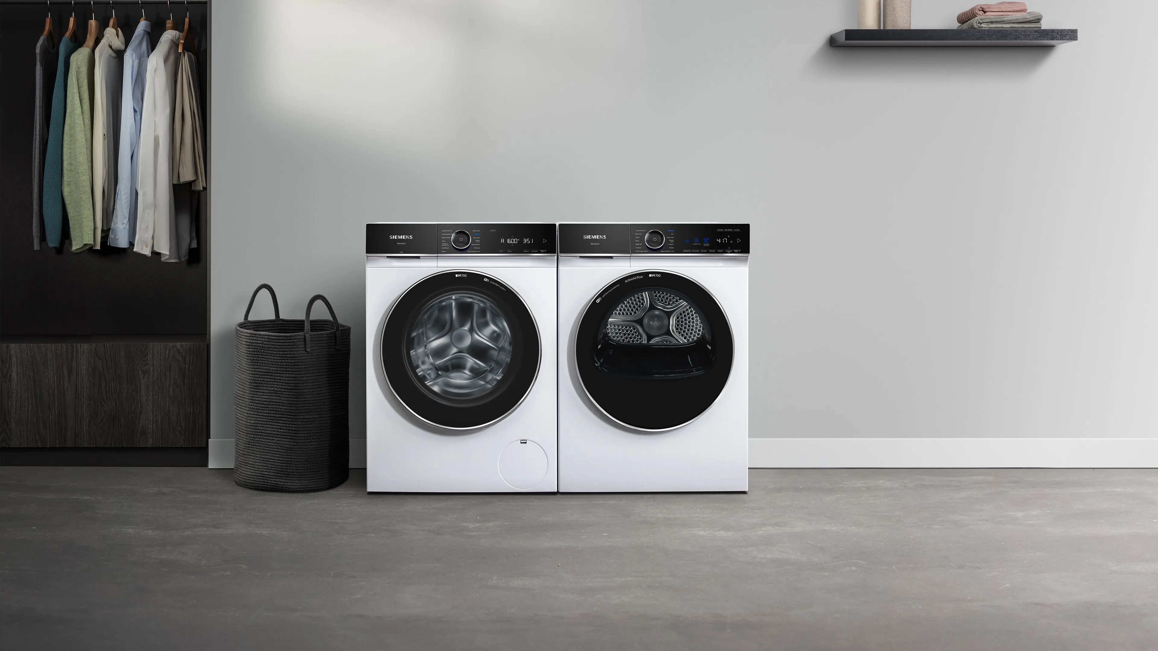 Chambre de lavage moderne avec lave-linge et sèche-linge primés, étagères avec serviettes et vêtements suspendus.