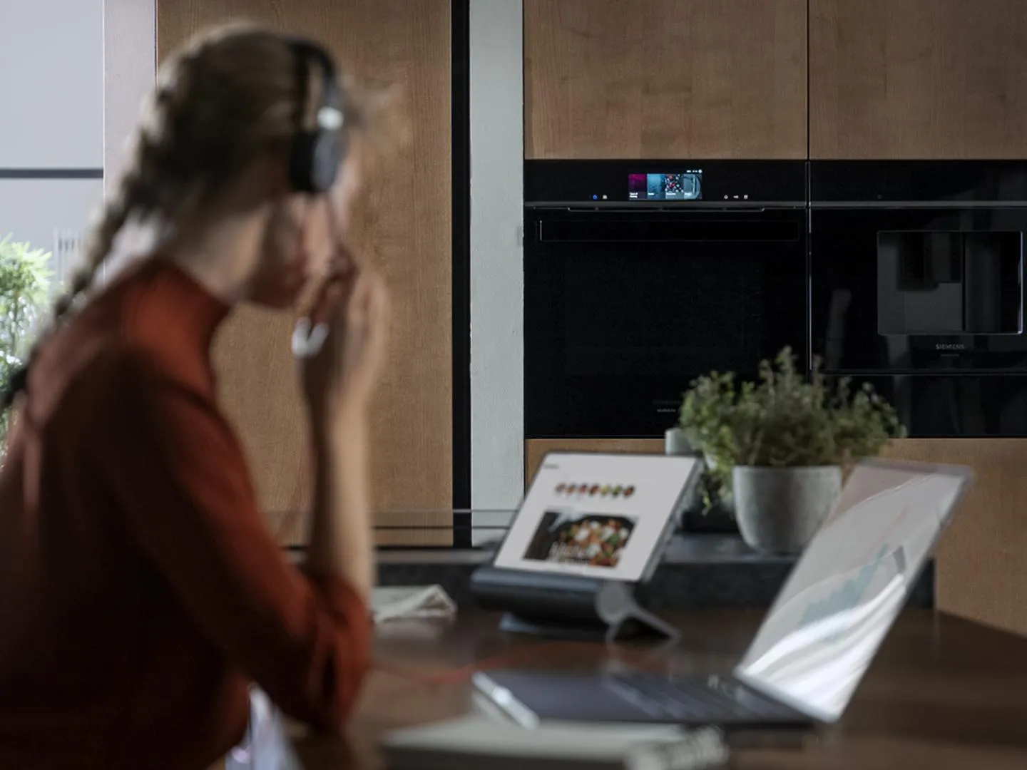 alt-Kobieta w sluchawkach pracuje w jadalni i używa aplikacji Siemens Home Connect