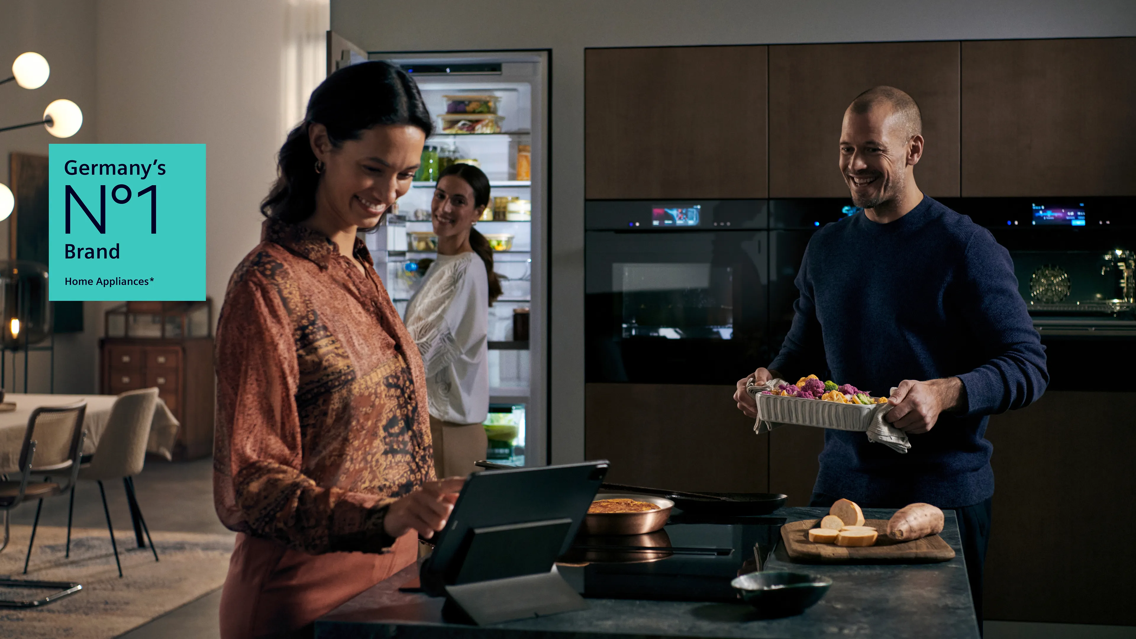 Three people enjoy drinks and snacks in a modern kitchen setting, with soft lighting and a stylish design.