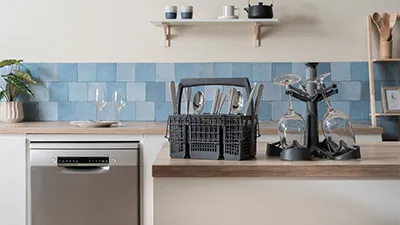 alt-Moderne keuken met een blauwe betegelde achterwand, met een vaatwasser. Het aanrecht heeft een bestekmand en een glazenhouder, samen met accessoires, wat een opgeruimde, georganiseerde sfeer oproept.