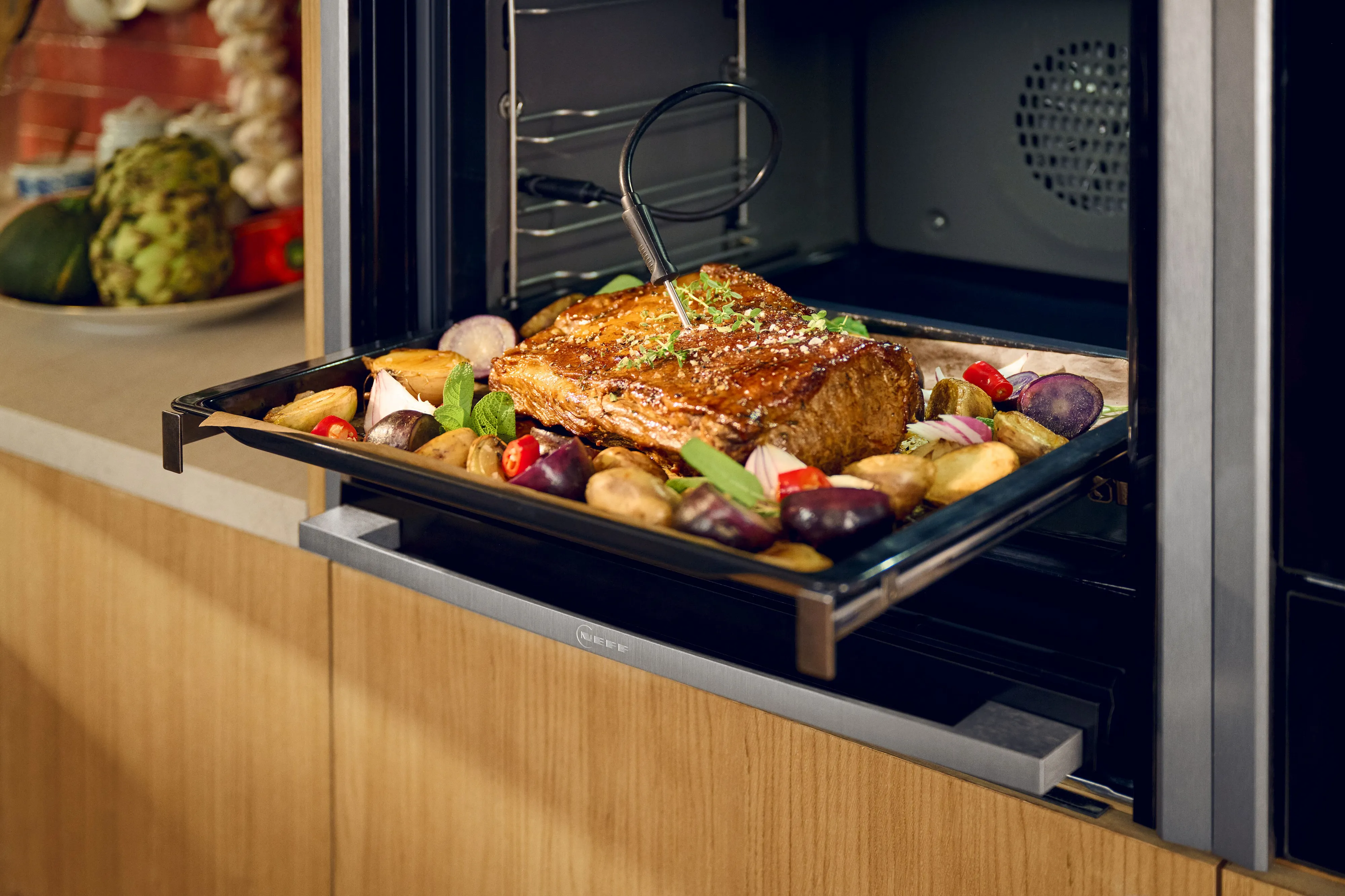 NEFF oven with meat probe inserted in tray of roast meat and vegetables