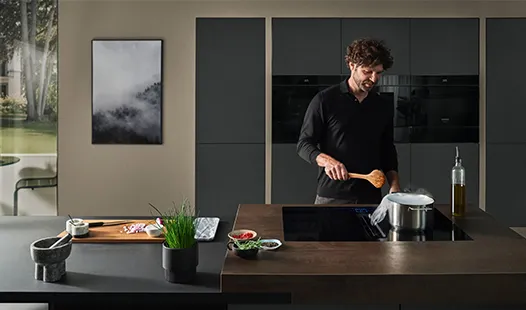 A man is preparing a meal in a sleek, modern kitchen with contemporary appliances and bright lighting.
