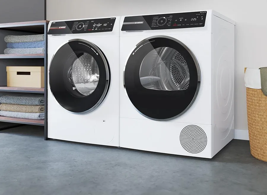 Modern washing machine and dryer set next to a wooden shelf with towels and a plant.