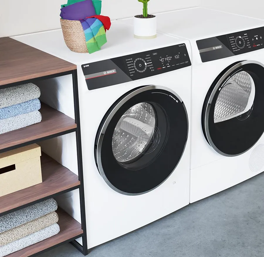 חדר כביסה חדיש עם יחידות כביסה ומייבש לבנות לצד מדף עץ מוערם במגבות וצמח. 