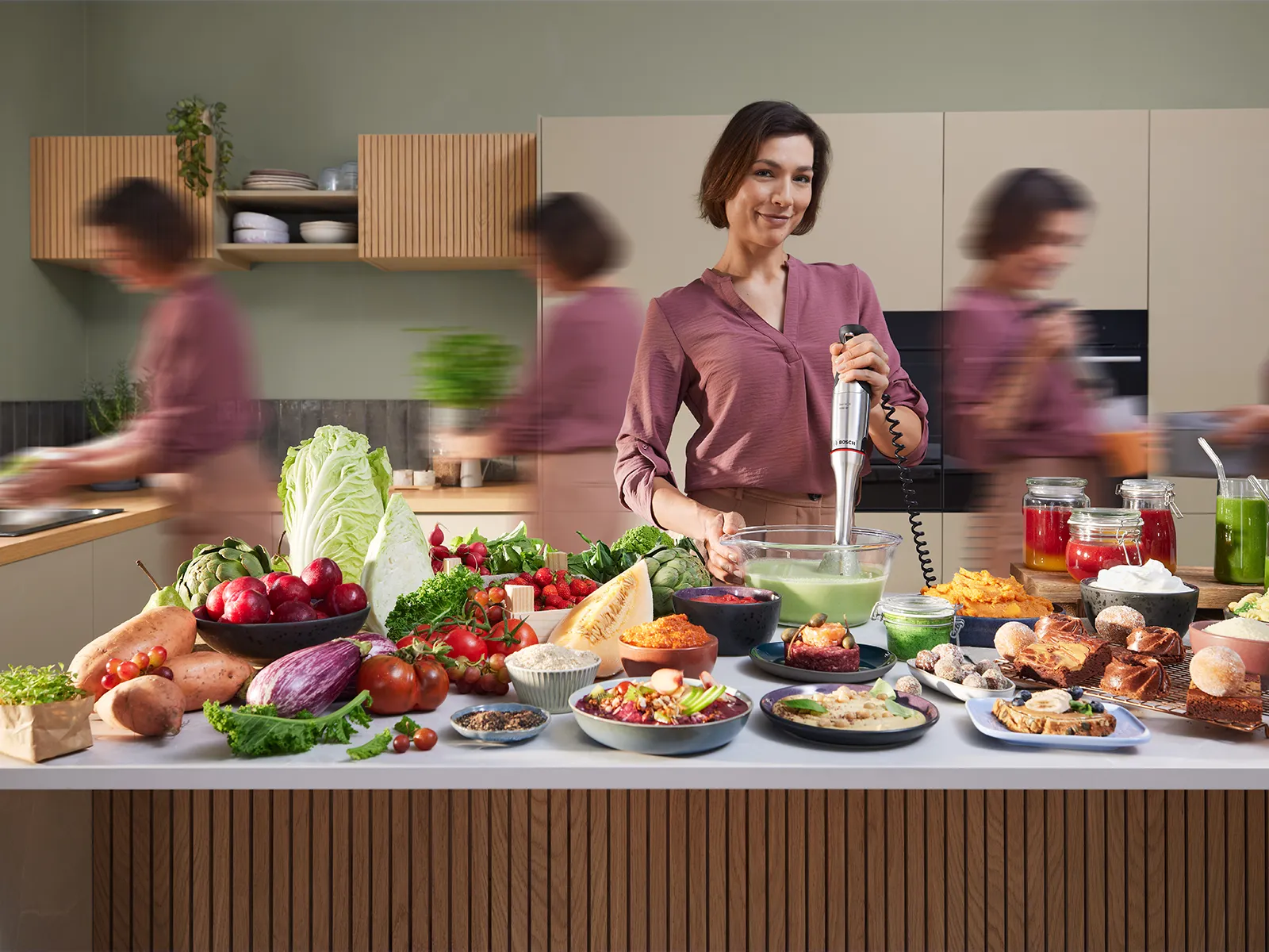 Una mujer sonriente está mezclando y versiones arrastradas de ella están ocupadas en una cocina, mientras que varias verduras y frutas se muestran en el mostrador.