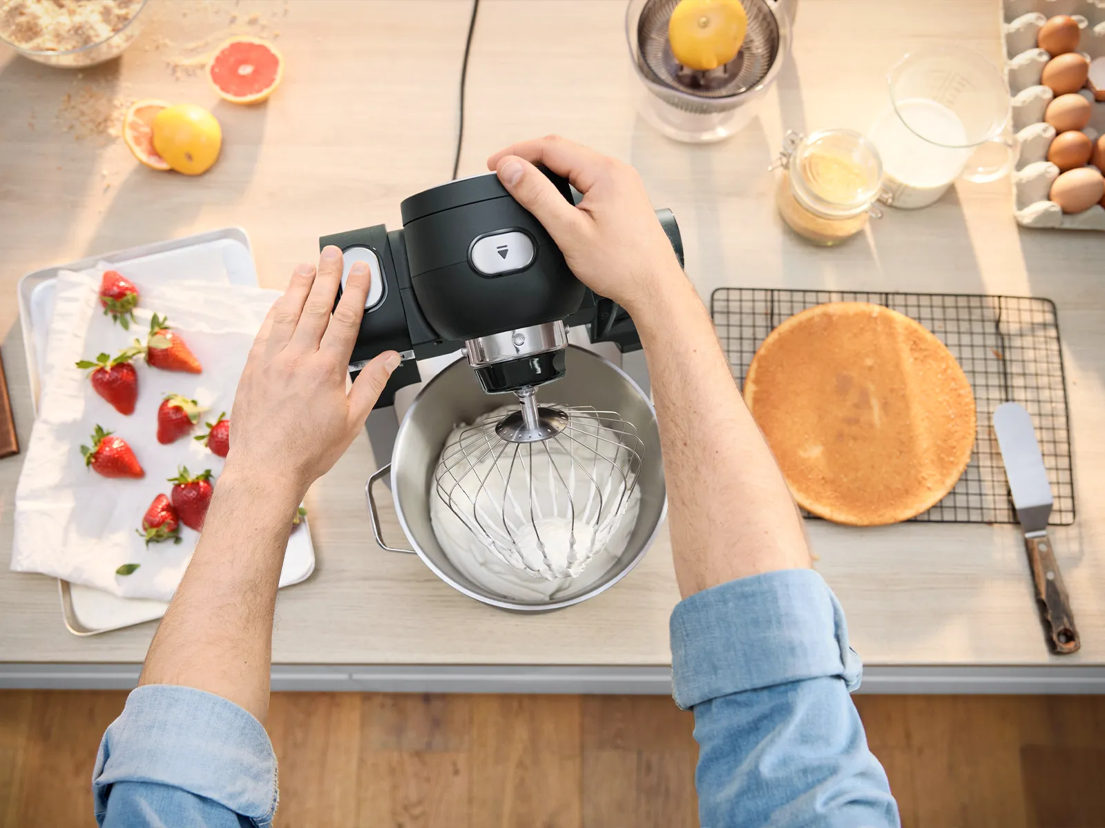 A person is operating a stand mixer on a kitchen counter with food and beverages around it.