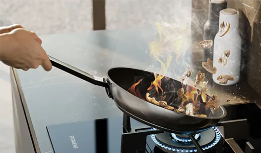  A person cooks food in a pan on a gas hob, focused on preparing a meal in a kitchen setting.  