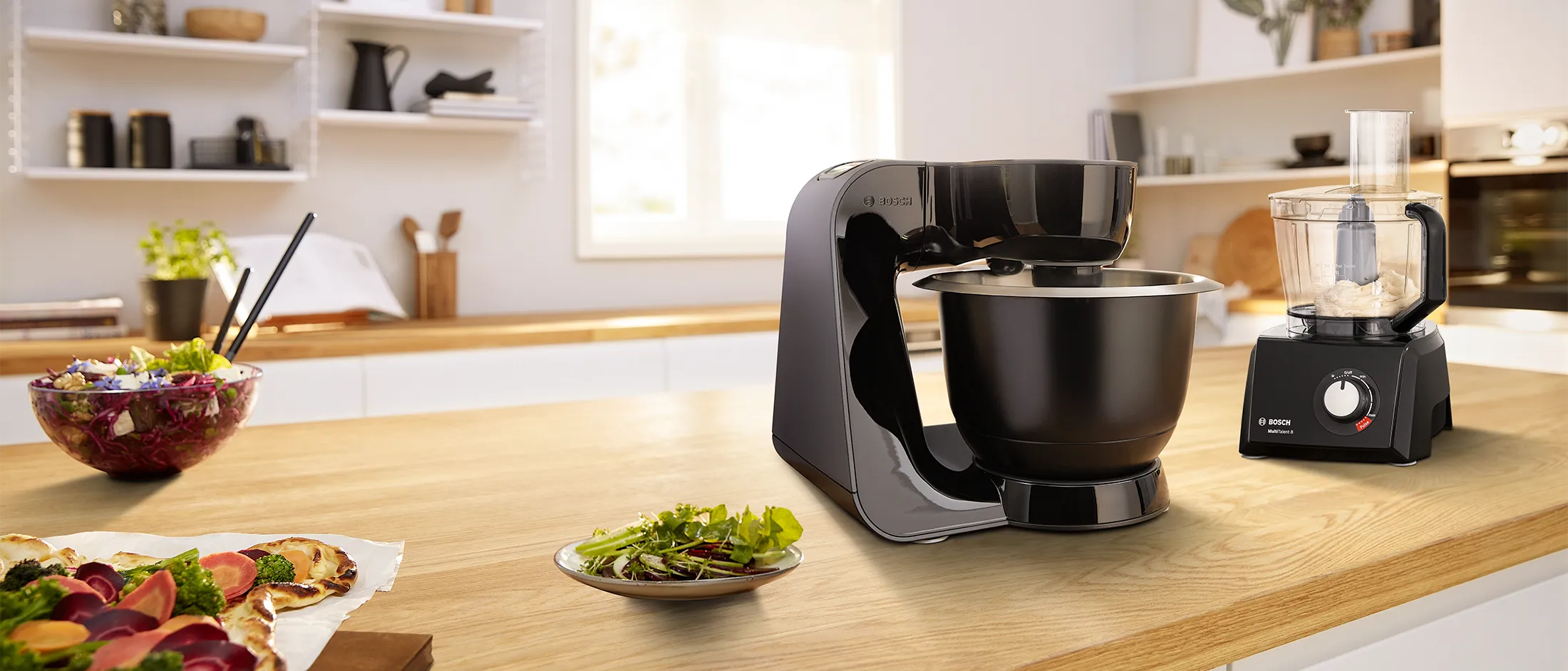 Bosch stand mixer and Bosch food processor on a wood worktop next to cake.