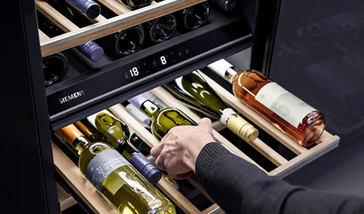 A person is opening a wine cooler filled with various bottles of wine. 
