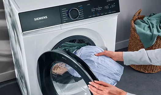 A person is placing a shirt into a front-loading washing machine for laundry.  