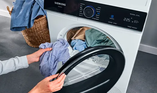 A person is loading a shirt into a tumble dryer.