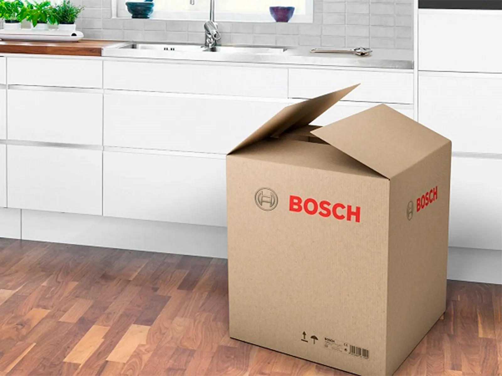 En kartong med Bosch-logotyp står på golvet i ett vitt kök.