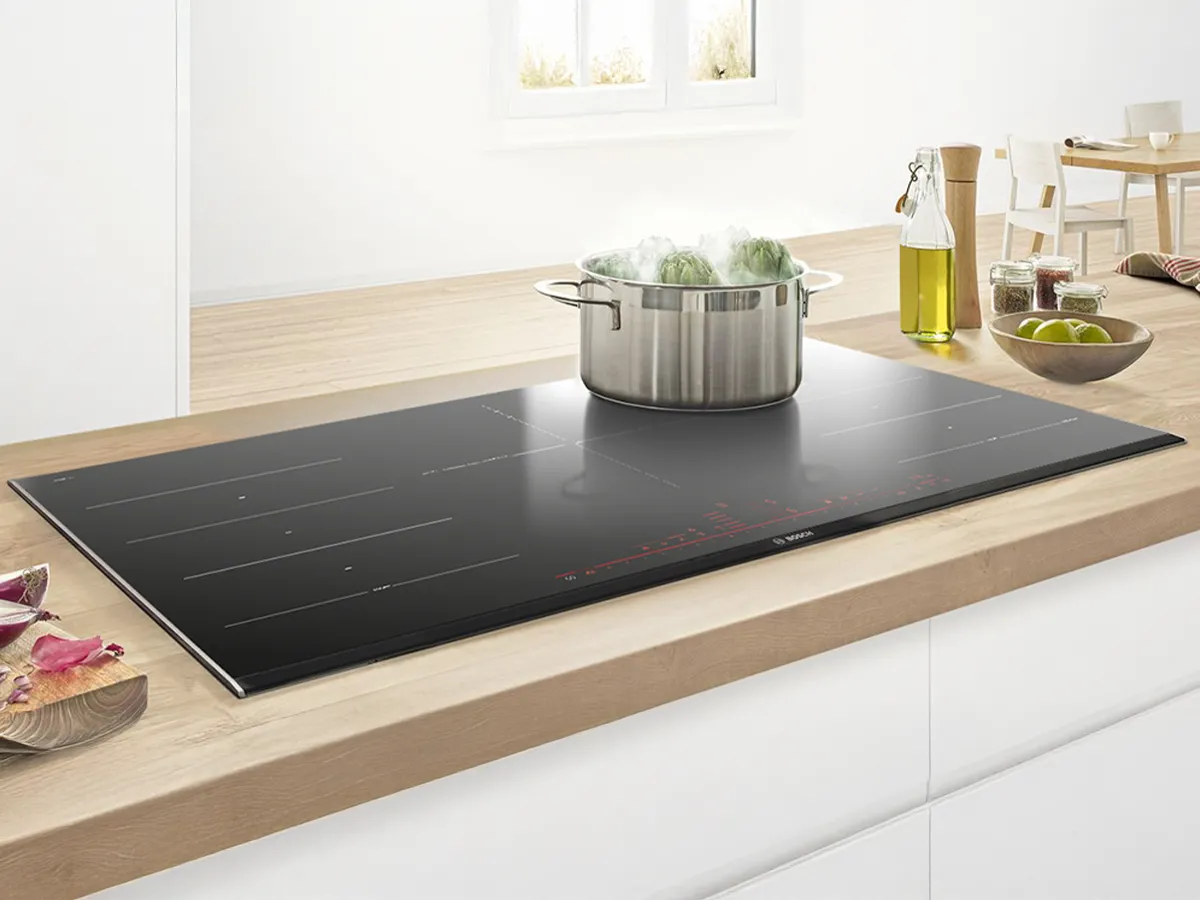 Modern kitchen with light wood cabinets, large window, dining table, and plants enhancing decor.