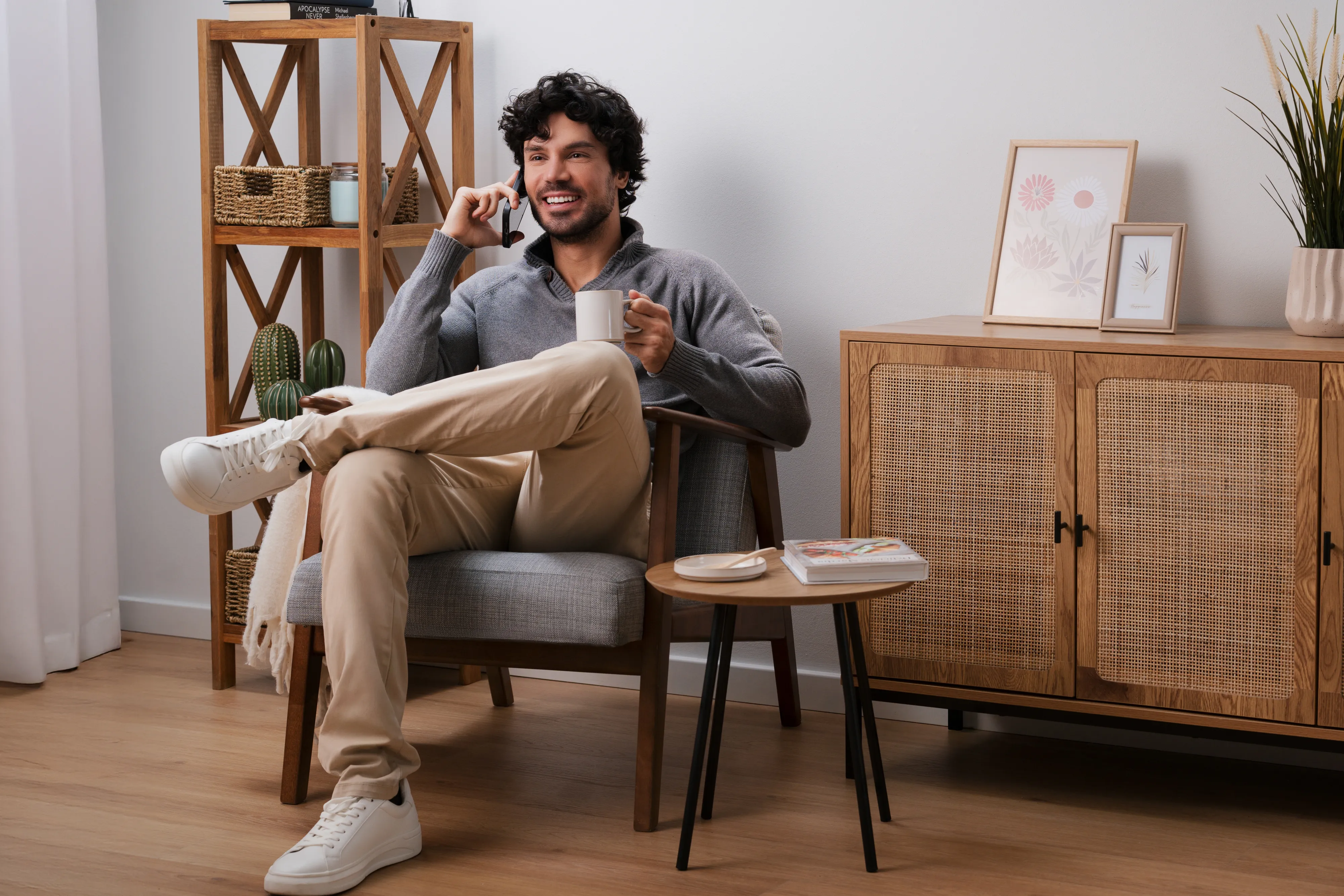 Een persoon zit comfortabel in een moderne stoel met een mok en neemt contact op met Bosch Service, met een stijlvolle houten kast en decoratieve planten in een gezellige kamer.