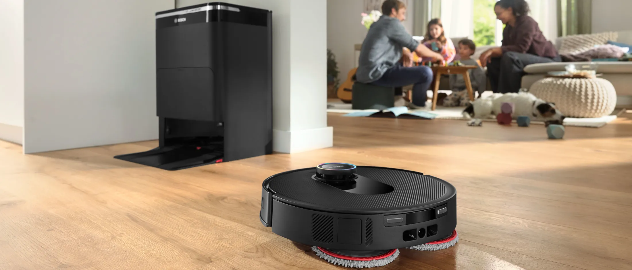 La familia prepara la comida, hay suciedad en el suelo y se ve claramente, el robot está limpiando el suelo.