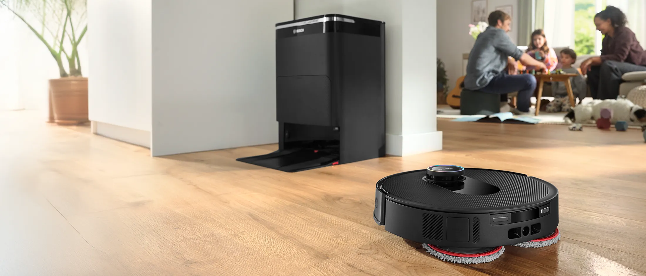 A sleek Bosch robotic vacuum rests gracefully on a polished hardwood floor, while a joyful family shares quality moments around the dining table in the background.