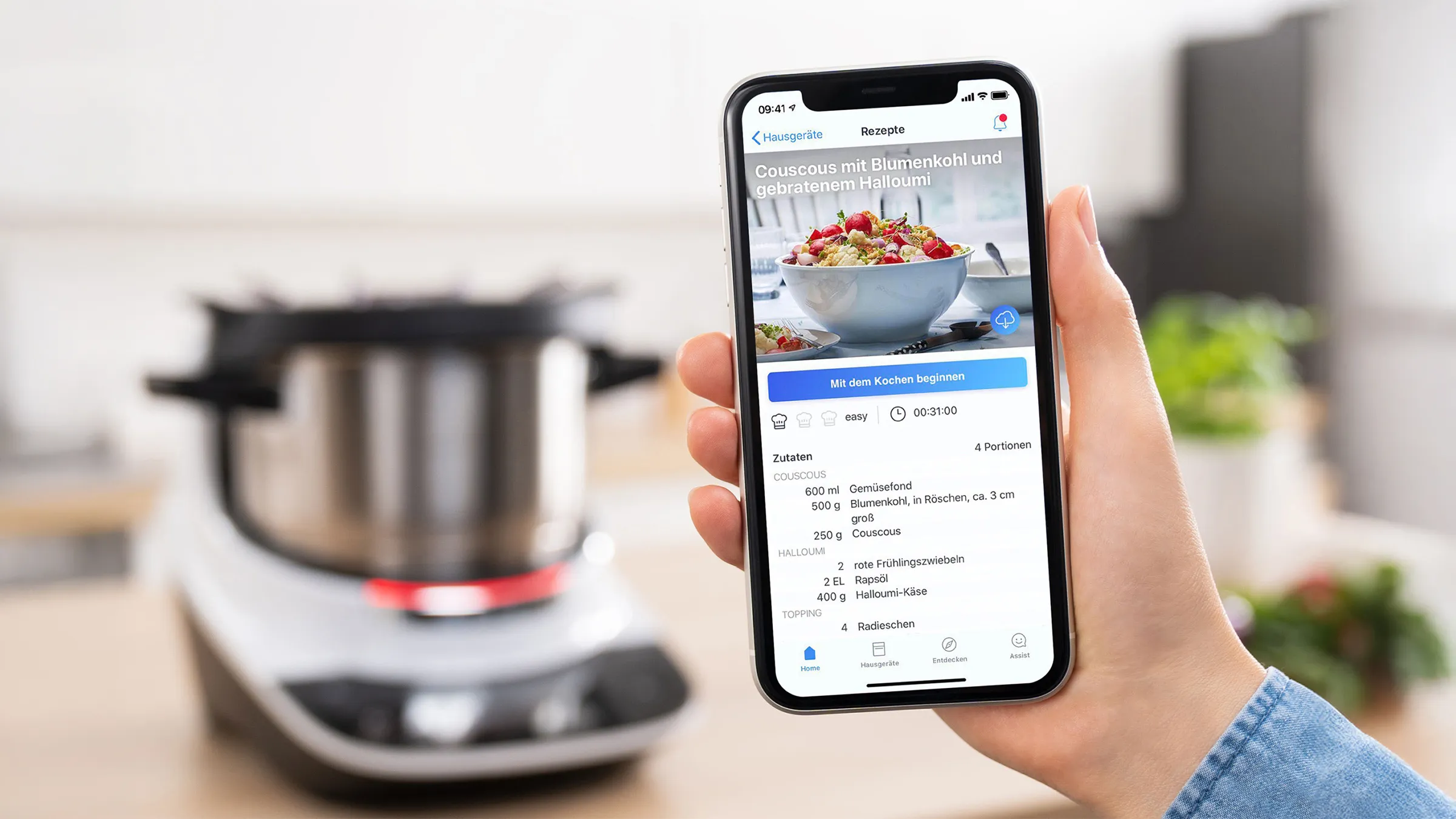 Smartphone mit digitalem Rezept in der Home Connect App vor einer Bosch Cookit Küchenmaschine.