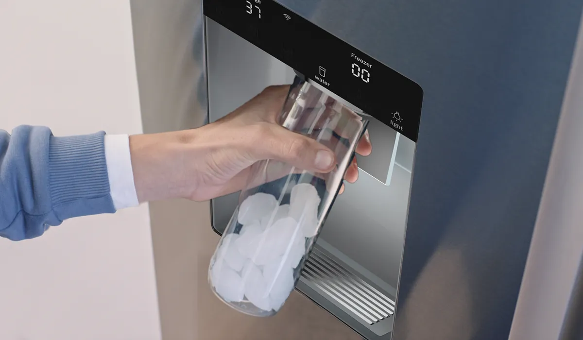 Hand holding a glass cup getting ice from a Bosch Stainless steel refrigerator