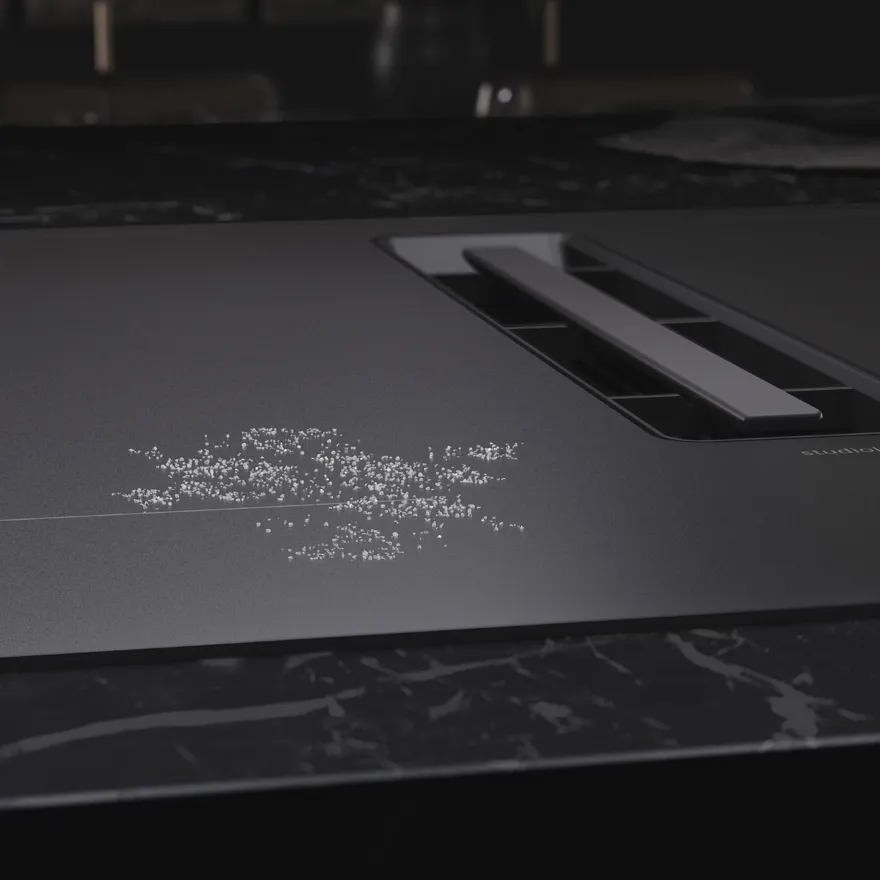 A modern stovetop with a sleek black surface and a small pile of white granules scattered near the burner controls.