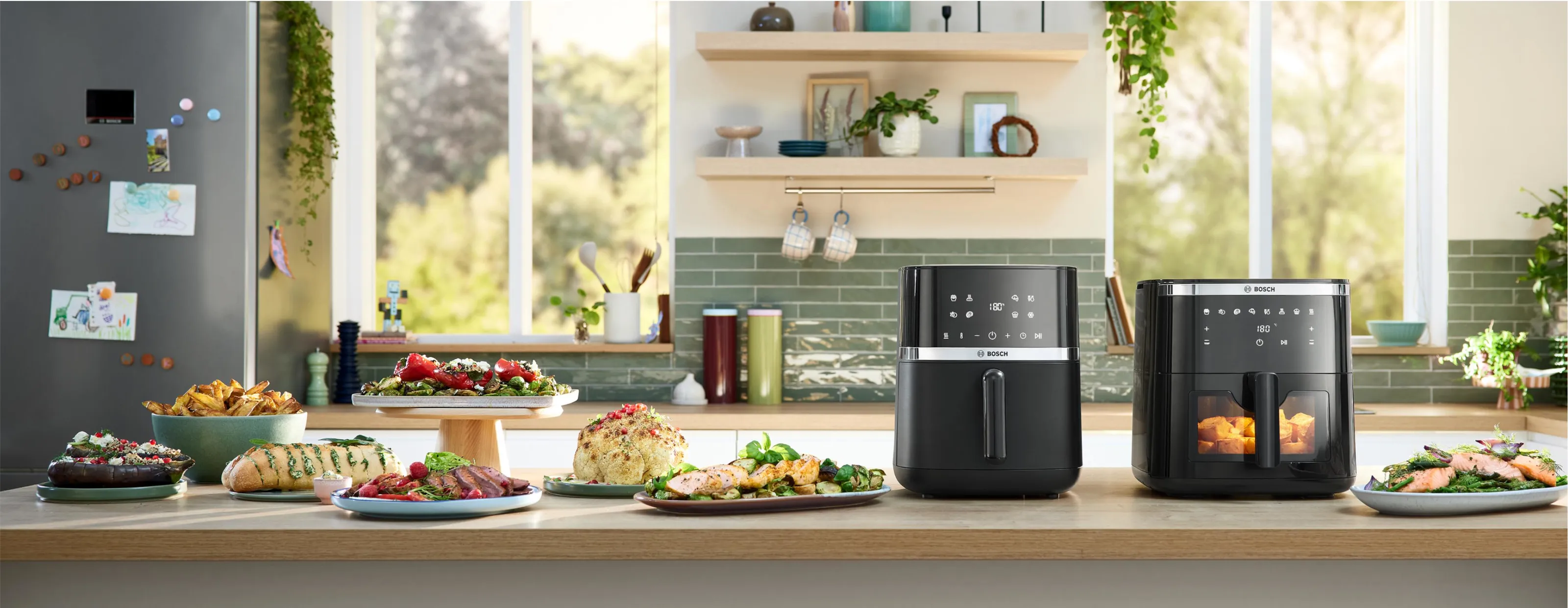 wei schwarze Bosch Air Fryer stehen auf einer Küchentheke, umgeben von verschiedenen frisch zubereiteten Gerichten wie Lachs, Steak, Salat und Kartoffeln.