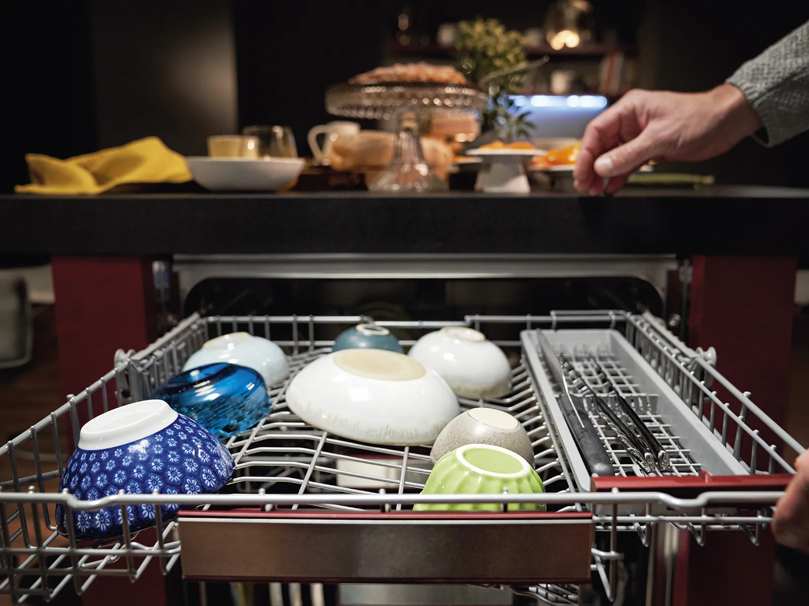 A silver dishwasher rack filled with colorful bowls and utensils.